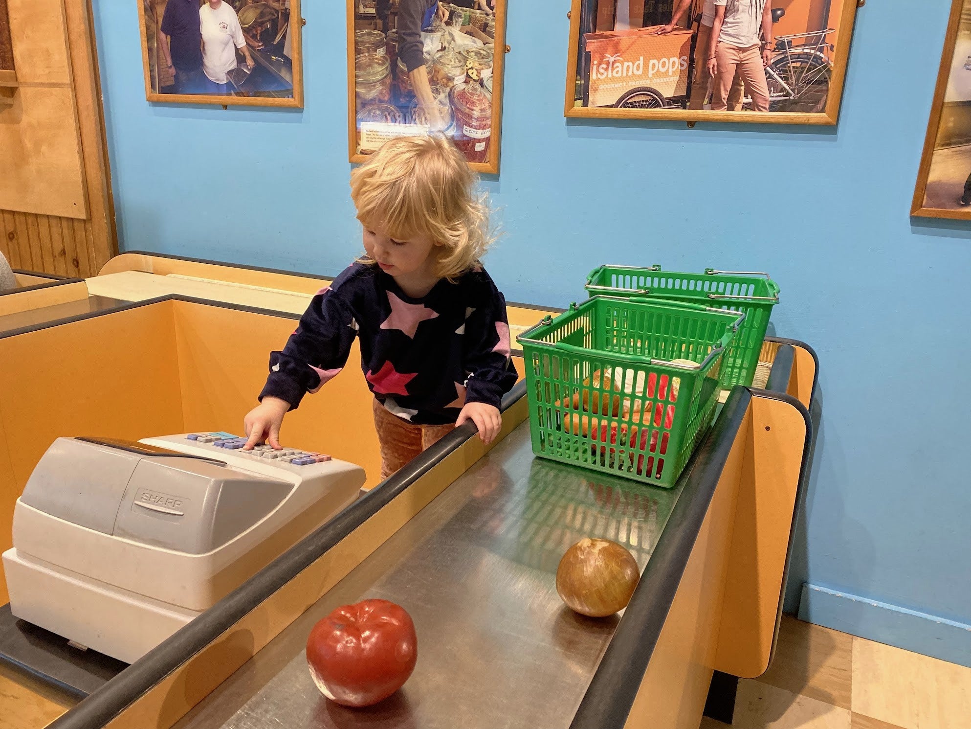 Girl in a pretend grocery store checkout playing as a cashier. Photo by the author